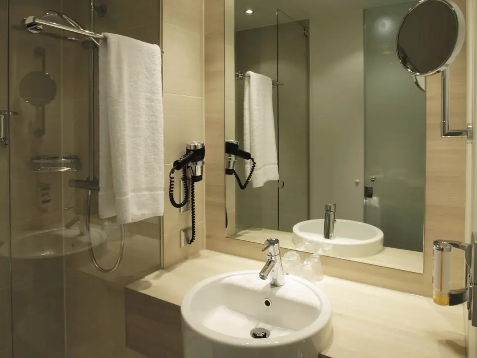 Badezimmer mit einer Dusche und einem Waschbecken. Über dem Waschbecken hängt ein großer Spiegel.