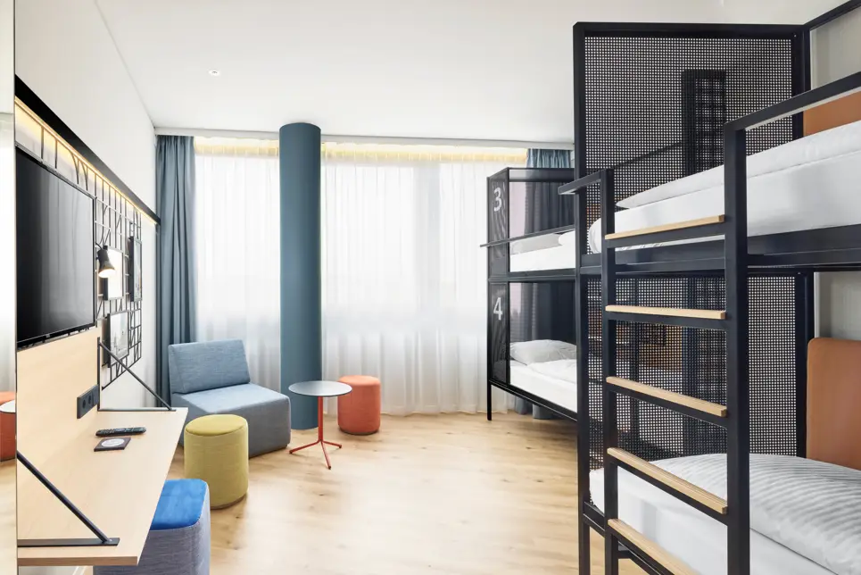 Etagenbetten im Hotelzimmer. In der Ecke ist eine Sitzecke mit einem Tisch.