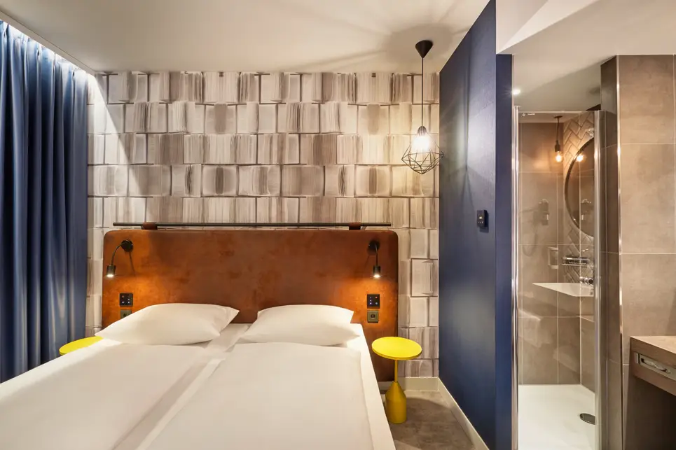 Doppelbett mit zwei Nachttischen und einer halben Trennwand zum offenen Bad.