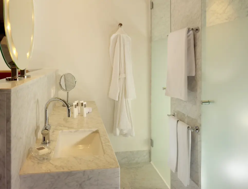 Waschbecken mit Marmoroptik auf der linken Seite. Auf der rechten Seite sind 2 Glastüren, ein Bademantel und ein Handtuch.