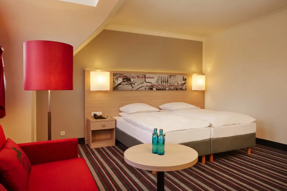 Großes Hotelzimmer mit einem Doppelbett. Im Vordergrund ist eine Sitzecke mit einer Stehlampe.