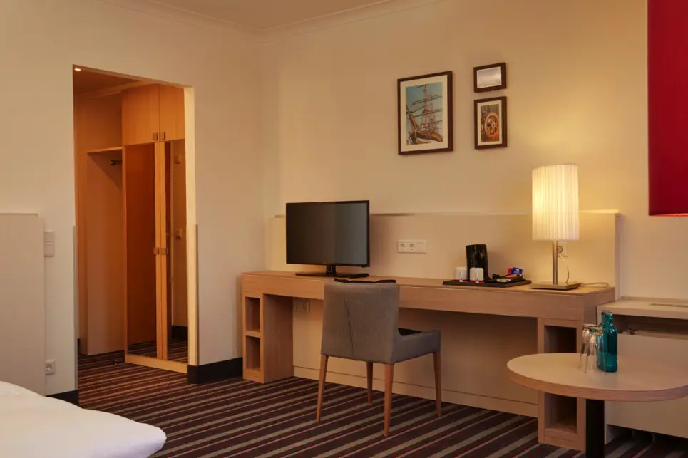 Schreibtisch im Hotelzimmer mit Stuhl und einem Fernseher. Über dem Schreibtisch hängt ein Bild.