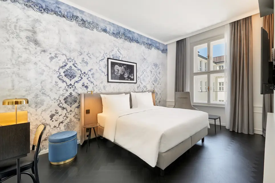 Doppelbett vor einer großen, blauen barocken Wand. Auf der linken Seite steht ein kleiner Hocker.