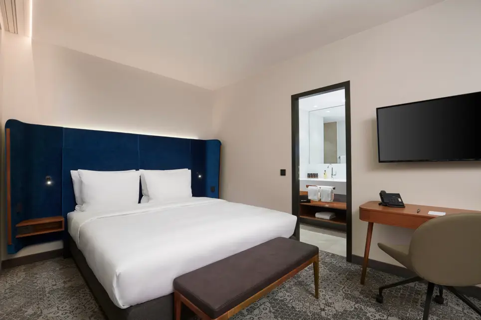 Ein Doppelbett mit einer Bettbank mit Blick in das Bad. Auf der rechten Seite ist ein kleiner Schreibtiisch mit einem Stuhl und einem Fernseher.