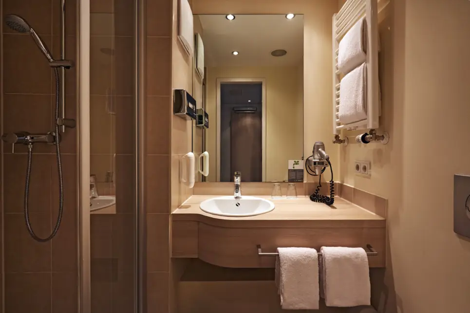 Badezimmer mit einer Dusche und einem Waschtisch. Über dem Waschtisch ist ein großer Spiegel und eine kleine Handtuchheizung.