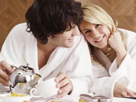 Ein Paar liegt im Bademantel auf dem Bett und Frühstücken.