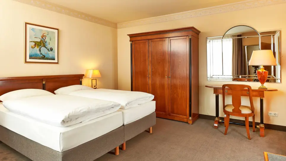 Hotelzimmer mit einem Doppelbett und einem großen Kleiderschrank daneben. Neben dem Kleiderschrank steht ein Schreibtisch.