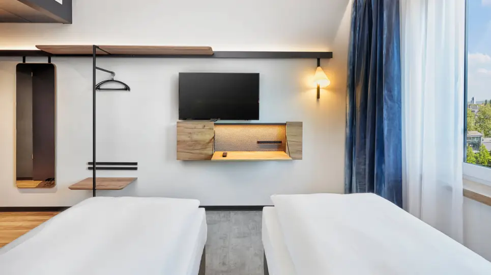 Twinbetten mit Blick auf den Fernseher und einer kleinen Gaderobe. Unter dem Fernseher ist ein kleiner Schreibtisch.