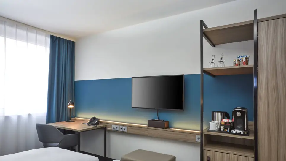 Hotelzimmer mit einem kleinen Schreibtisch, einem kleinen Schrank und einem Fernseher an der Wand.