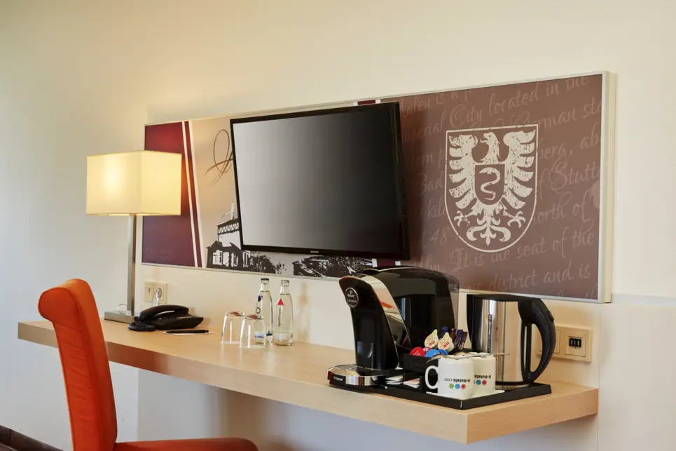 Schreibtisch mit einer Kaffeemaschine. Darüber hängt ein Fernseher.