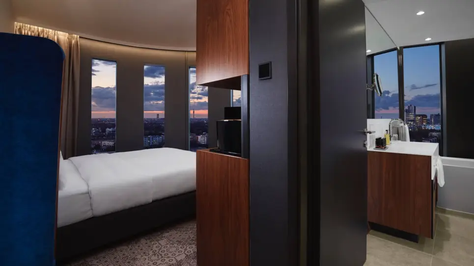 Auf der linken Seite steht ein Ausschnitt vom Bett. Auf der rechten Seite ist ein dunkelbrauner Schrank mit einem Spiegel.