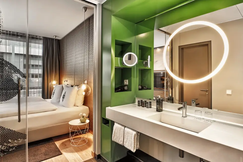 Waschtisch mit einem großen, runden Spiegel. Neben dem Waschtisch ist ein großer Spiegel an der Wand, der das Doppelbett spiegelt.