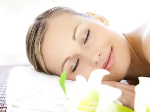 Kopf einer Frau, die auf einer Liege entspannt. Im Vordergrund liegen Lilien.