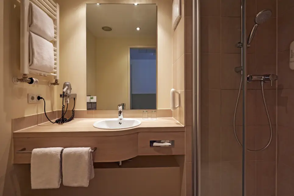 Badezimmer mit einem Waschbecken und Handtüchern. Neben dem Waschbecken steht eine Dusche.