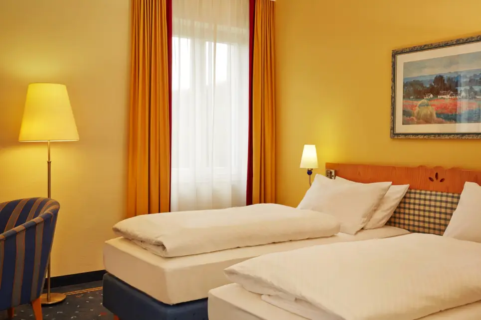 Twinbettem vor einem Fenster. Über den Betten hängt ein Bild.