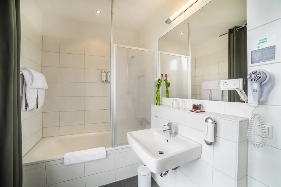 Badezimmer mit einer Duschbadewanne und einem Waschbecken. Über dem Waschbecken hängt ein großer Spiegel und ein Fön daneben.