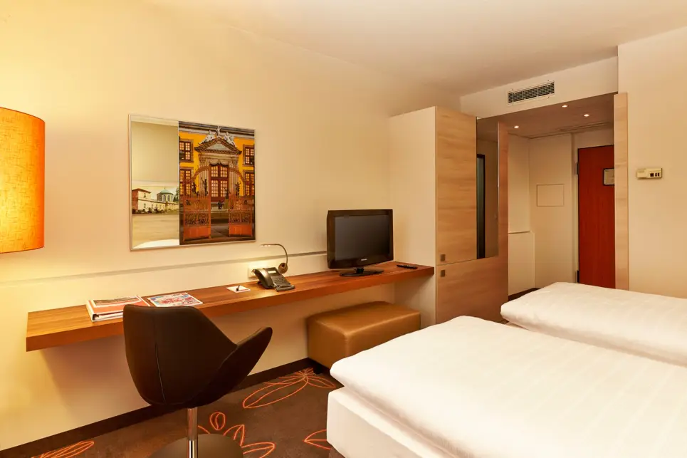 Vor zwei Einzelbetten steht ein Schreibtisch mit einem Fernseher und einem Sessel.