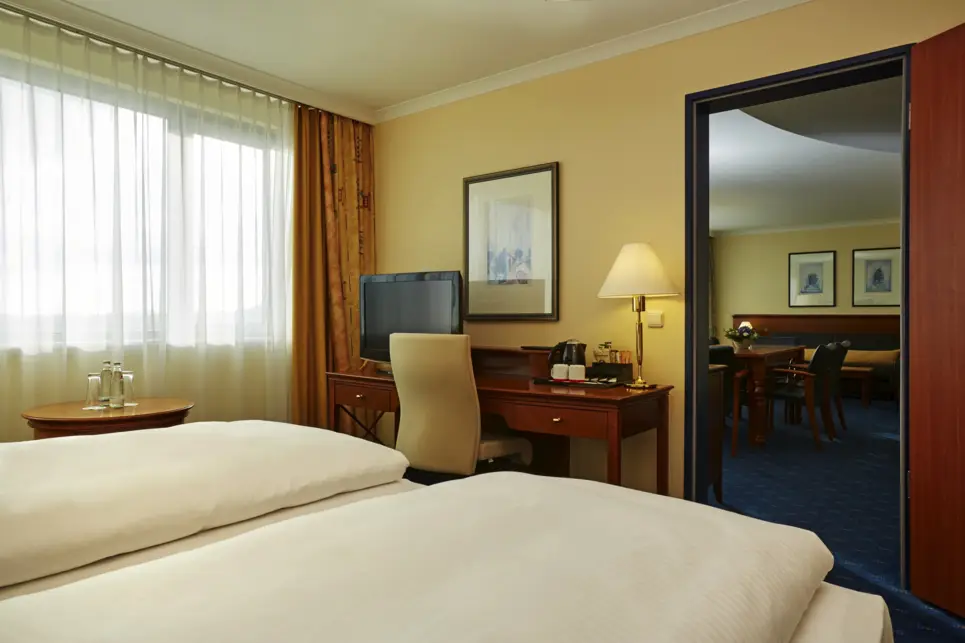 Schlafbereich der Grandsuite mit einem Schreibtisch. Durch eine Tür schaut man in den Wohnbereich.