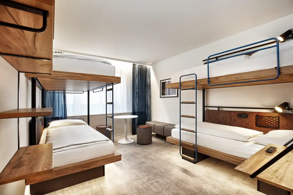 Vierbettzimmer mit Etagenbetten. In der Ecke ist eine kleine Sitzecke mit einem Tisch.