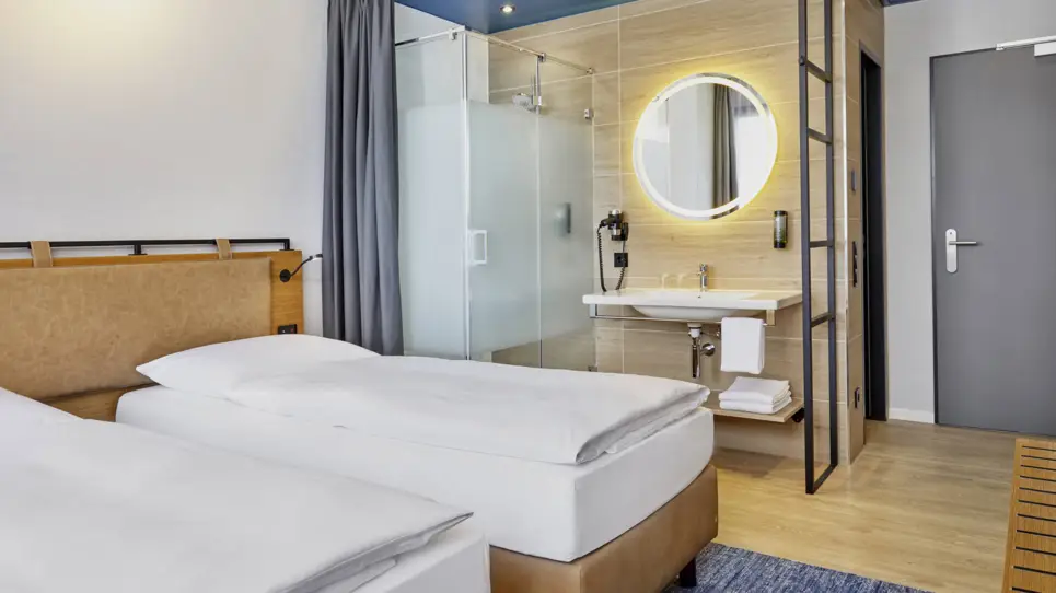 Twinbetten im Hotelzimmer mit einem offenen Bad mit Waschbecken und einer Dusche.