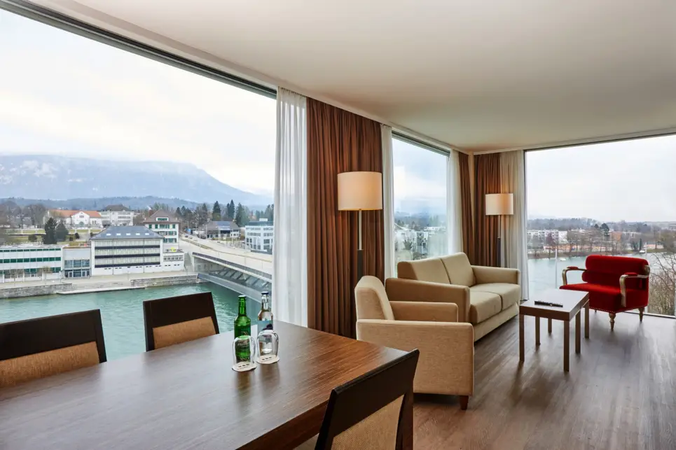 Großzügiger Wohnbereich in einer Suite mit einem Esstisch und Sitzgelegenheiten. Die Suite hat mehrere große Fenster.