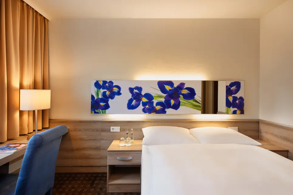 Doppelbett im Hotelzimmer mit einer beleuchteten Rückwand.