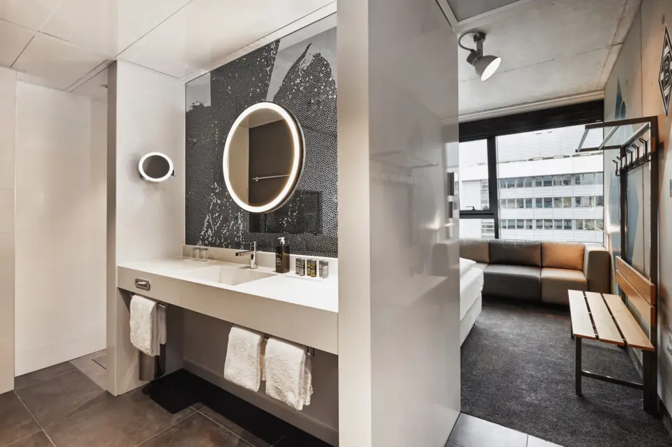 Hinter dem Bett ist mit Trennwänden ein Waschbecken mit einem runden Spiegel.