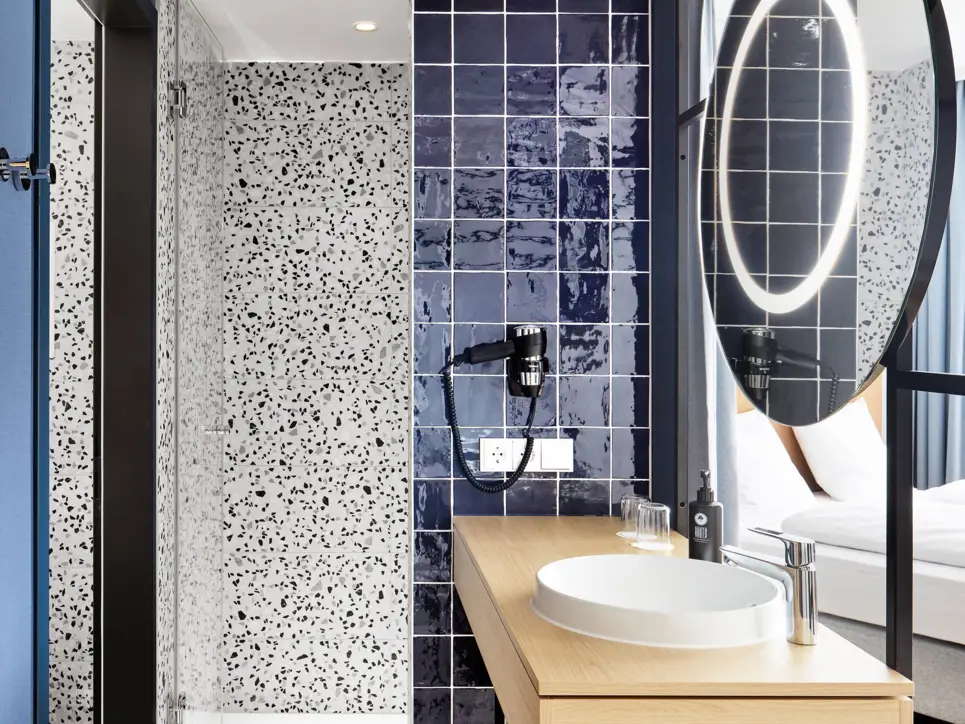 Offenes Badezimmer mit einem Waschbecken. Daneben ist eine Dusche.