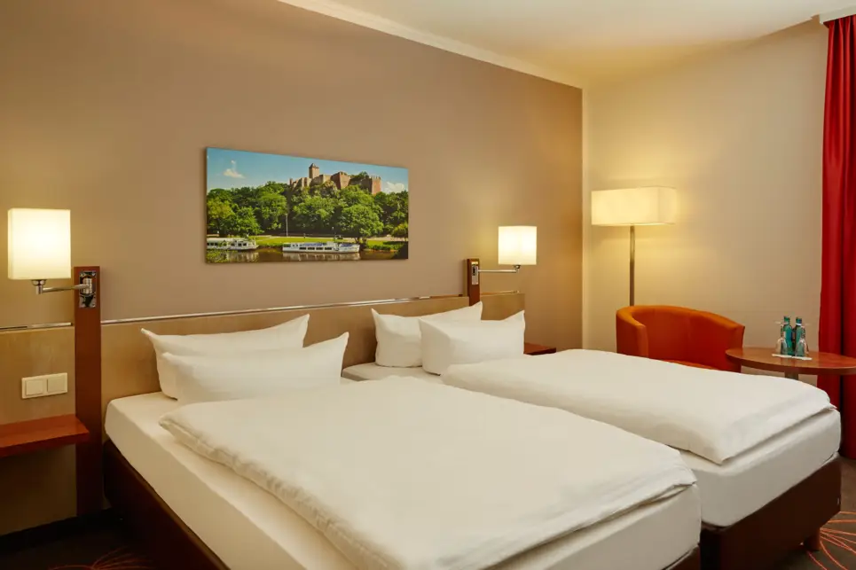 Doppelbett mit Nachttisch und einem Sessel neben den Bett. Über dem Bett hängt ein Bild.