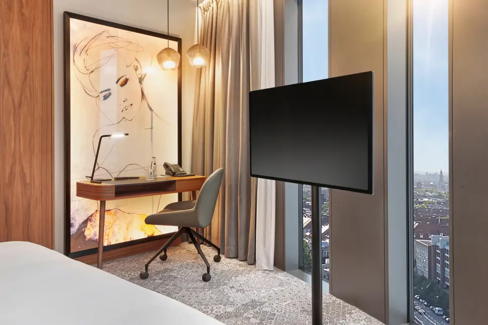 Detailierter Blic kauf den beleuchteten Schreibtisch mit einem Bild. Auf der rechten Seite steht ein Fernseher auf einem Ständer vor bodentiefen Fenstern.