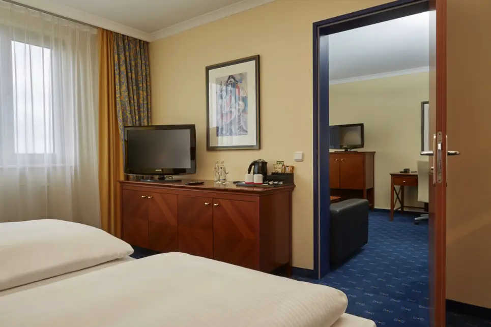 Blick vom Schlafbereich in der Suite in den Wohnbereich. In der Ecke steht ein Fernseher.