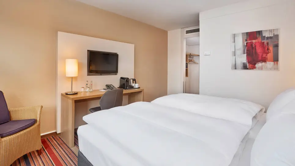 Hotelzimmer mit einem Doppelbett. Vor dem Bett steht ein Schreibtisch und ein Stuhl.