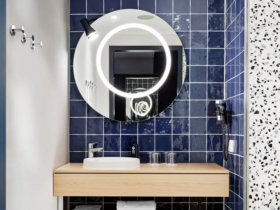 Waschtisch mit einem großen, runden Spiegel darüber. An der Wand hängt ein Föhn.