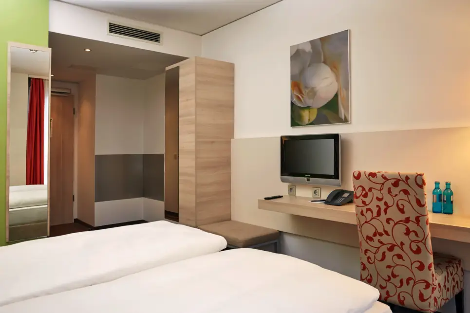 Blick vom Bett auf einen kleinen Schreibtisch mit einem Fernseher. Neben dem Schreibtischsteht ein Kleiderschrank.