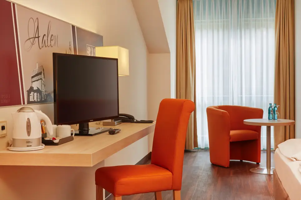 Schreibtisch mit einem Fernseher. Neben dem Fernseher steht ein Wasserkocher.