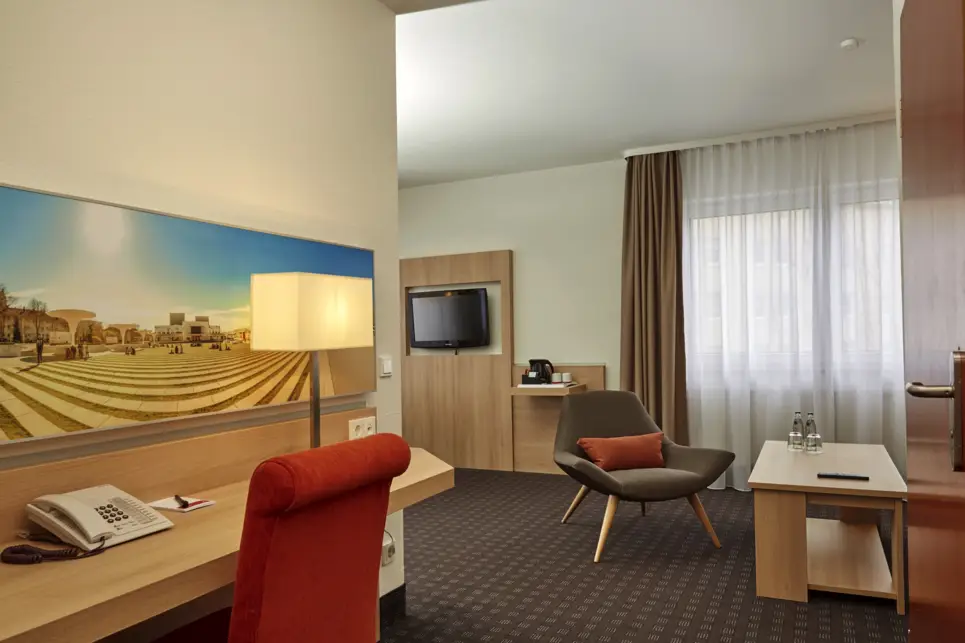 Blick vom Hotelzimmerflur in das Hotelzimmer mit einem Stuhl und einem Schreibtisch.