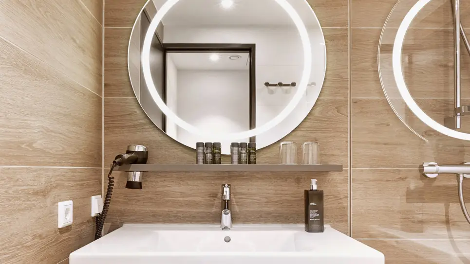 Badezimmer mit einem Waschbecken und einem großen, runden beleuchteten Spiegel.