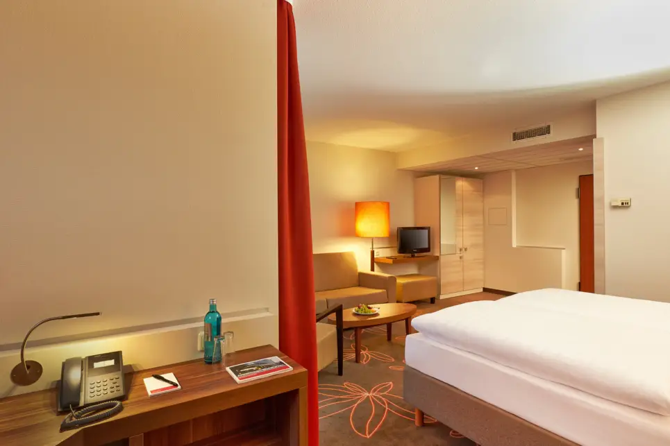 Kleiner Schreibtisch mit einem Telefon neben dem Bett. Vor dem Bett steht ein kleiner Tisch mit einer Couch.