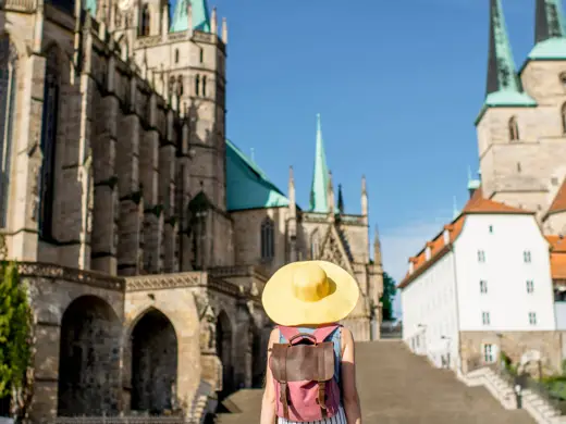 Eine Frau mit einem großen gelben Hut steht auf dem Domplatz und schaut zum Erfurter Dom.
