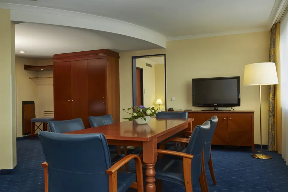 Großzügige Grandsuite mit einem Konferenztisch und einem großen Schrank. Vor dem Tisch steht ein Fernseher.
