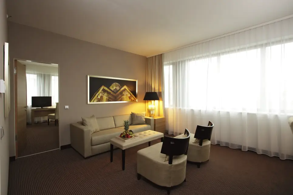 Sitzecke im Wohnbereich eines Hotelzimmers mit einer Couch und zwei Sesseln. 