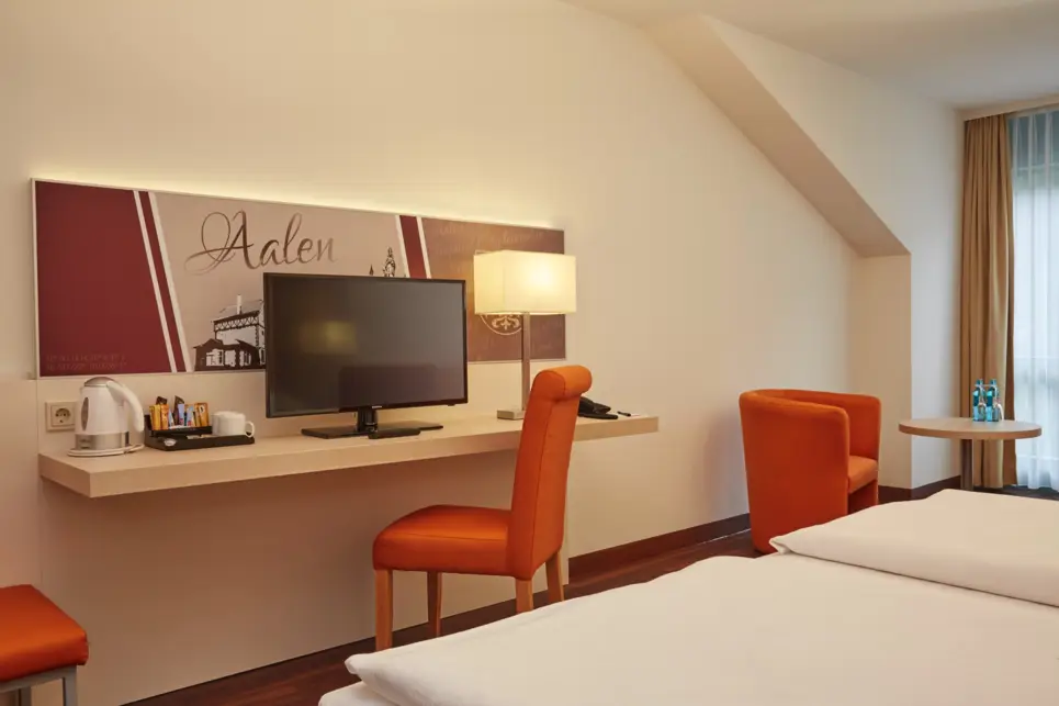 Schreibtisch mit einem Fernseher im Hotelzimmer. Davor steht ein Doppelbett.