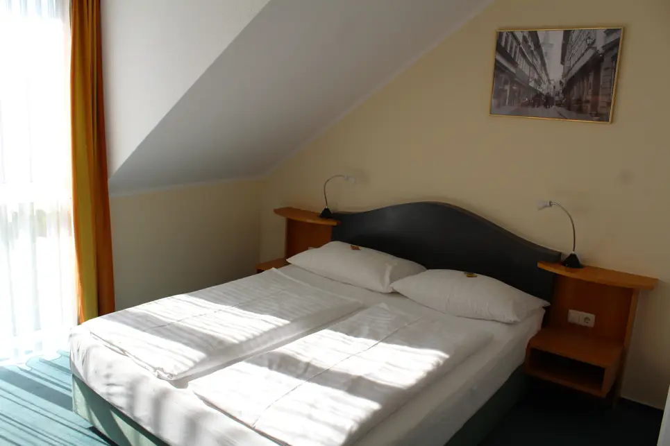 Doppelbett im Hotelzimmer vor einem großen Fenster.