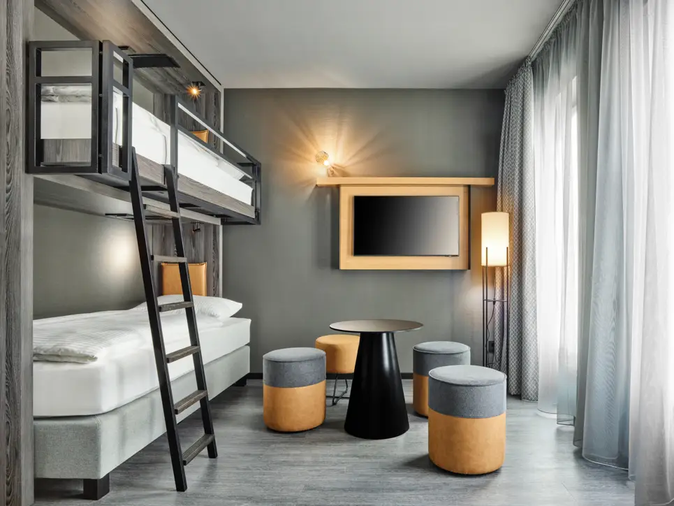 Hotelzimmer mit einem Etagenbett auf der linken Seite und einer kleinen Sitzgruppe auf der rechten Seite.