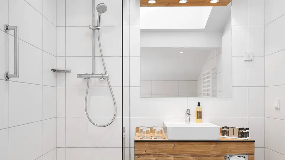 Badezimmer mit einem Waschbecken und einem großem Spiegel darüber. Auf der linken Seite ist eine Dusche.