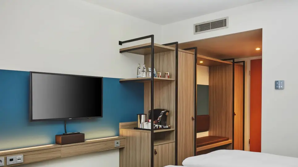 Blick im Hotelzimmer auf den kleinen Vorflur. Vor dem Flur steht ein kleiner Schrank und ein Fernseher.