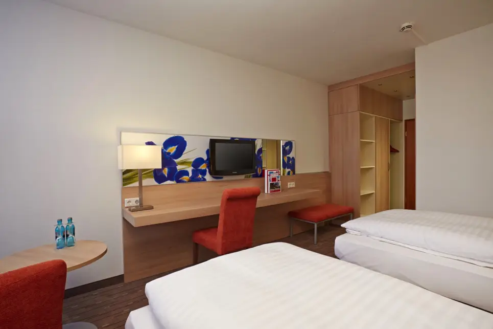 Twinbetten vor einem Schreibtisch. Nebne dem Schreibtisch ist eine Gaderobe.