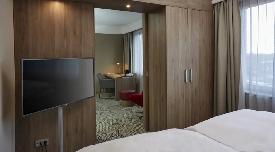 Blick vom Bett auf einem Fernseher mit Standfuß und aus einer Tür in einen anderen Raum.