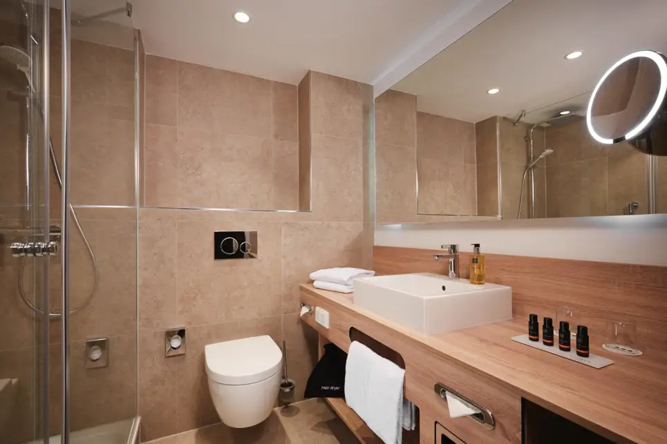 Hellbraunes Badezimmer mit einem großem Spiegel, einer Dusche und Holzbadmöbeln.