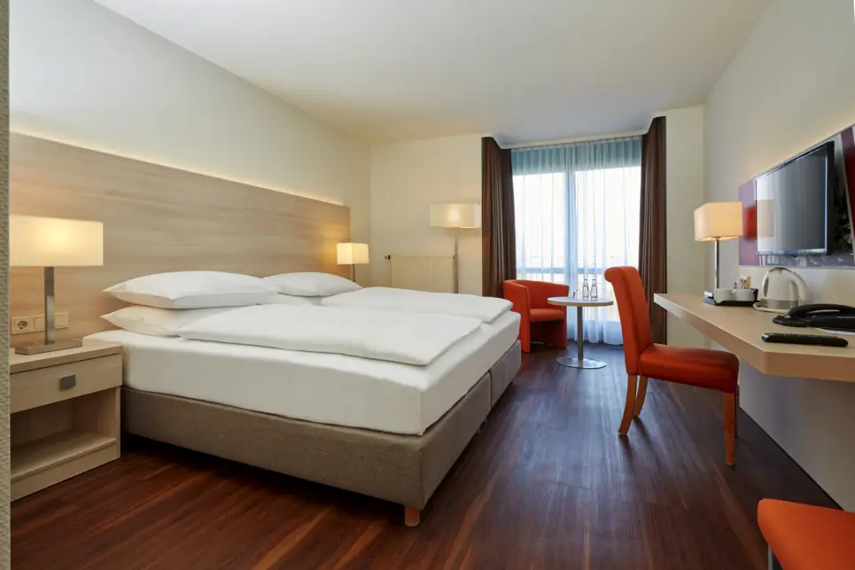 Großes Hotelzimmer mit einem großen Doppelbett. Vor dem Bett steht ein kleiner Schreibtisch.